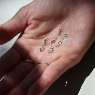 Hand holding small silver charms on a plain background