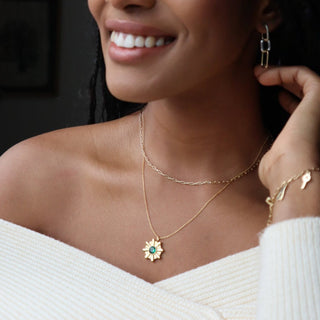 Woman wearing the Amelia Sunray Pendant with emerald green crystal, layered with a delicate chain necklace.