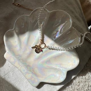 Estelle Pearl Necklace displayed on an iridescent seashell dish, showcasing its elegant design and charm.