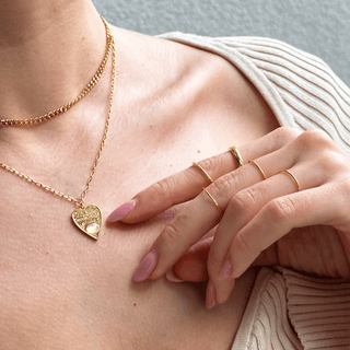 Woman wearing golden Mystic Oracle Pendant with heart charm and layered rings on finger, stylish and elegant.