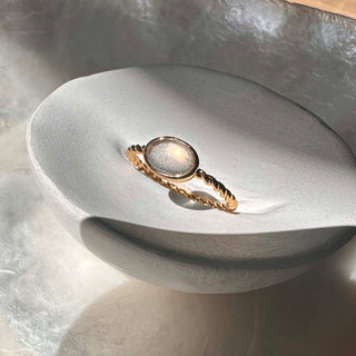 Dainty Nebula Labradorite ring on a textured bowl, showcasing its color-shifting glow and twisted gold band.