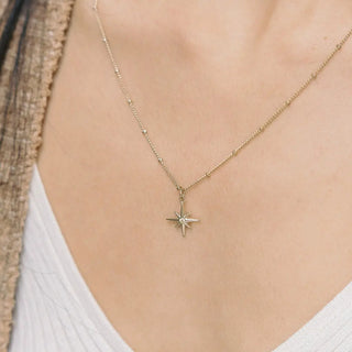 Close-up of the North Star Necklace featuring a golden starburst charm and a tiny central crystal.
