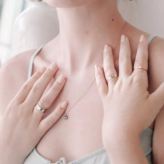 Delicate woman wearing the Ode to Rose Necklace with a blue alexandrite pendant, showcasing elegant rings and soft skin tones.