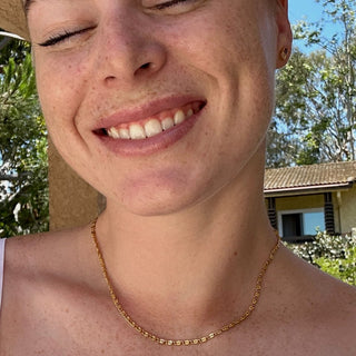 Smiling person wearing a stylish Snail Chain Necklace with whimsical spiraled links, showcased in a sunny outdoor setting.