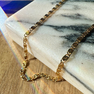 Glimmers of gold on a stunning Snail Chain Necklace with spiraled links, resting on a marble surface.