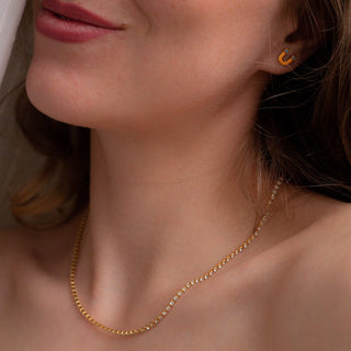 Close-up of a woman wearing a twinkle tennis chain necklace with sparkling crystals and a stylish gold earring.