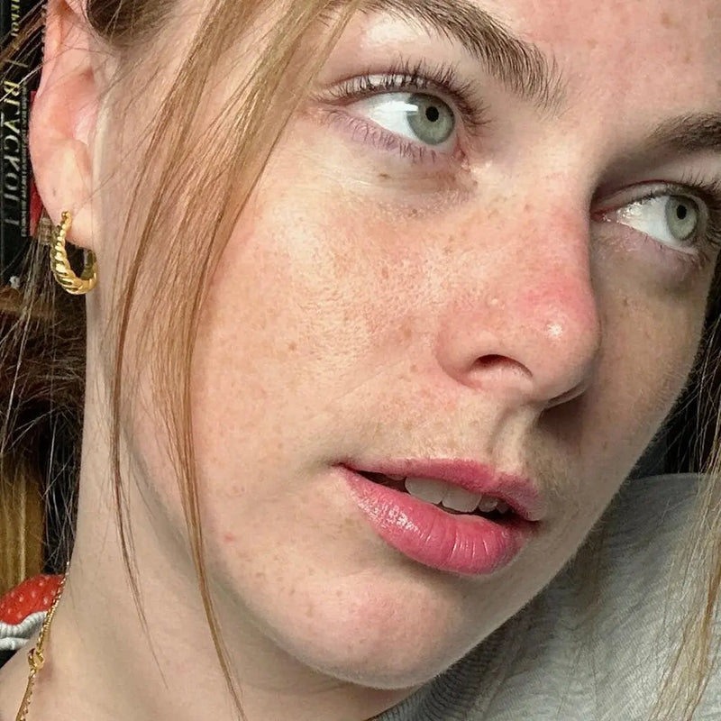 Close-up of a model showcasing golden croissant hoops earrings, featuring natural beauty and light makeup.