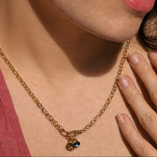 Close-up of a person wearing a gold necklace with an evil eye charm and whoa face charm