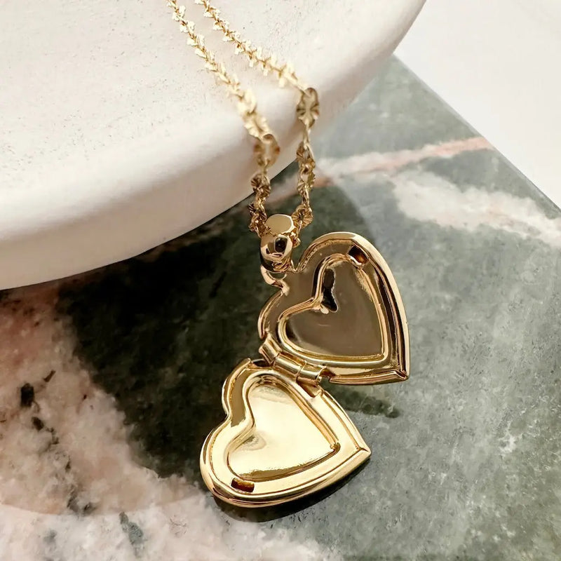 Gold heart locket necklace on a marble surface, showcasing a romantic design with a delicate chain.