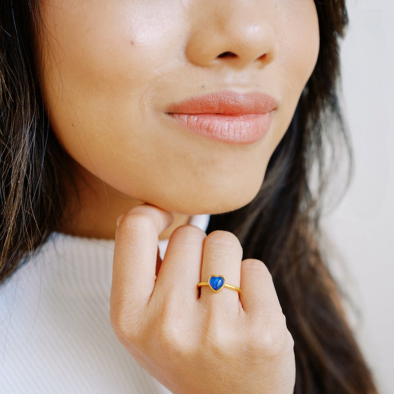 A woman showing off a heart-shaped mood ring, featuring a blue stone, highlighting its stylish design.