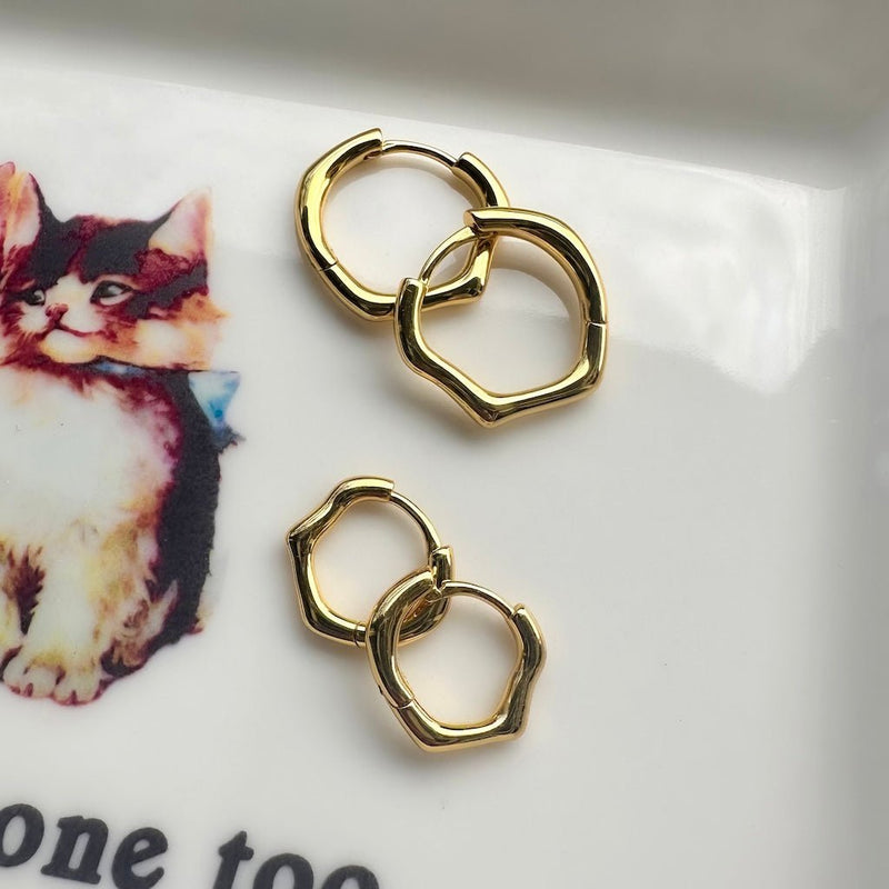 Elegant organic-shaped gold hoops, available in small and medium sizes, displayed on a patterned plate.
