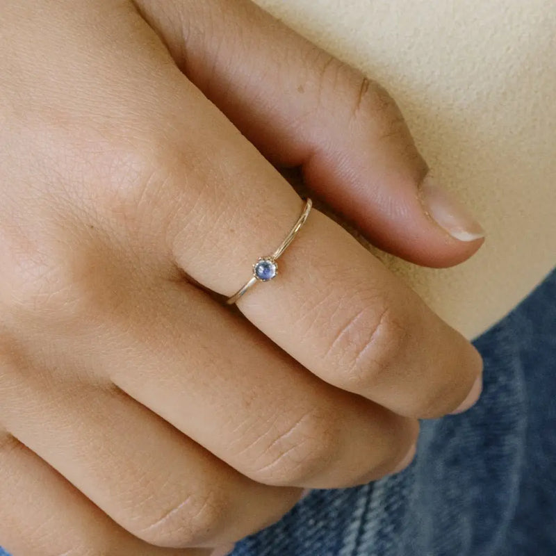 Person wearing a gold vermeil solar mood ring with a blue color-changing stone on their finger.