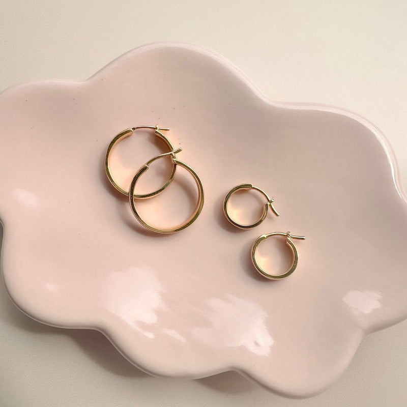 Gold Wheel Hoops in small and large sizes displayed on a pink dish, perfect for effortless, stylish looks.